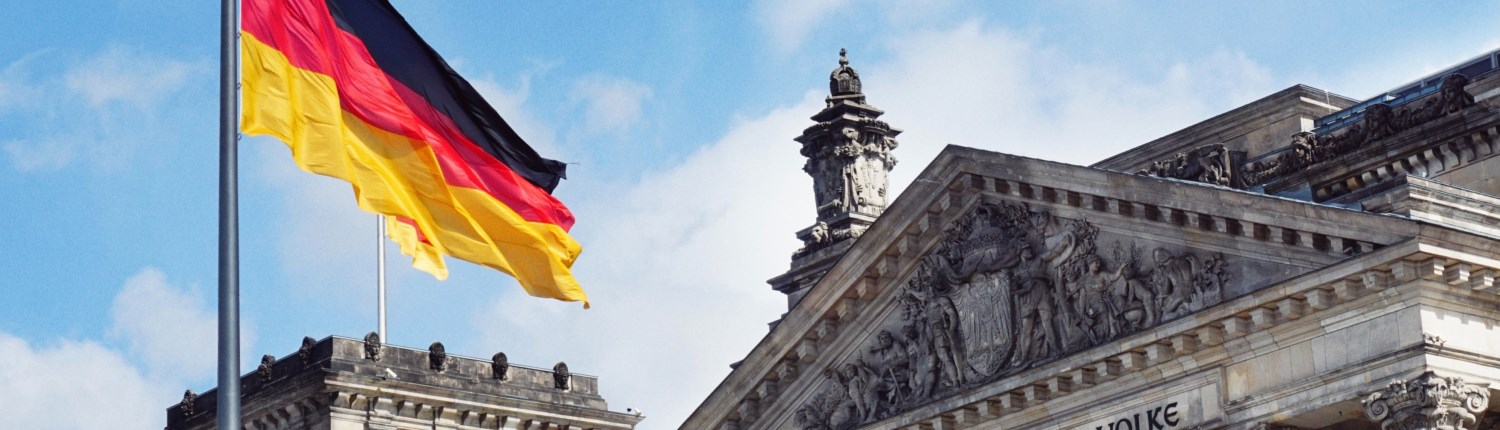 The German flag flies from a flagpole in front of an ornate baroque-style building