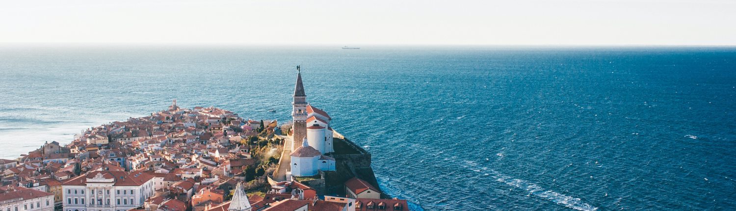 Red rooves and a bell tower occupy a small peninsula which juts out into the Adriatic Sea in Piran, Slovenia