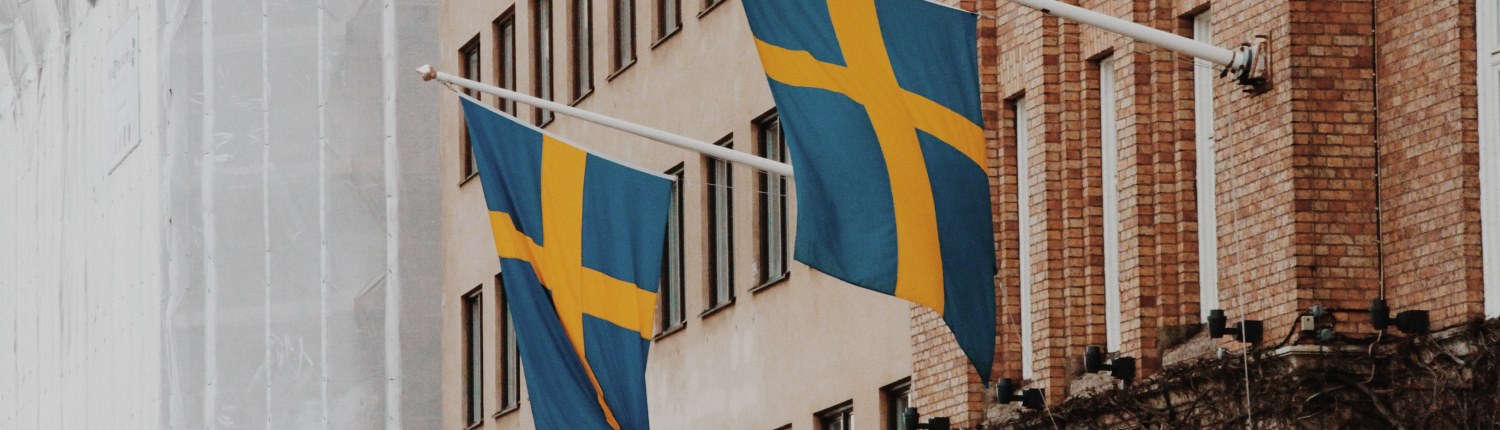 Two Swedish national flags hang from flagpoles mounted on a red brick building